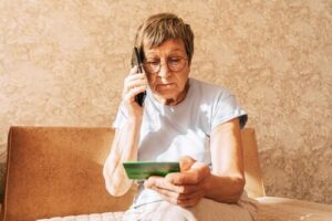 elderly woman on phone holding credit card while seated indoors